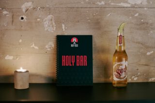 Innenraum des Holy Taco: Kerze vor einer Wand mit Totenkopf‑Deko, in violettem Licht erstrahlt. Mit einer Flasche Sol Cerveza mit einer Limettenscheibe. In der Mitte die Getränkekarte mit der Aufschrift 